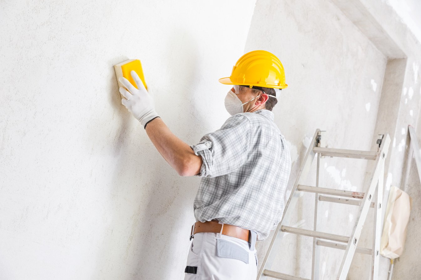 Builder sanding and smoothing newly plastered wall